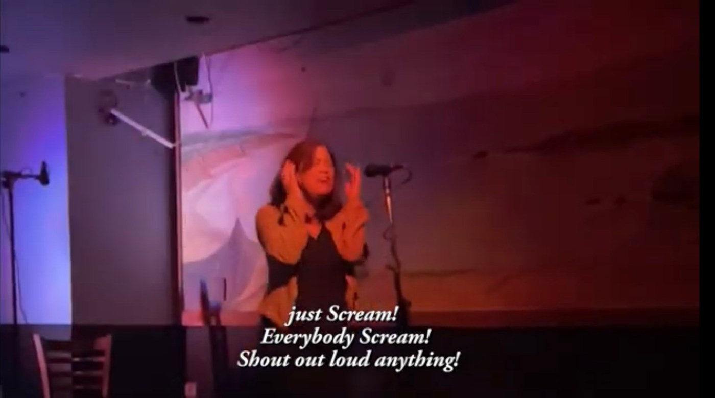Screenshot of video. I’m performing and singing an acapella lyric at an open mic. The lyrics are “Scream! Everybody Scream. Shout out loud everything.”